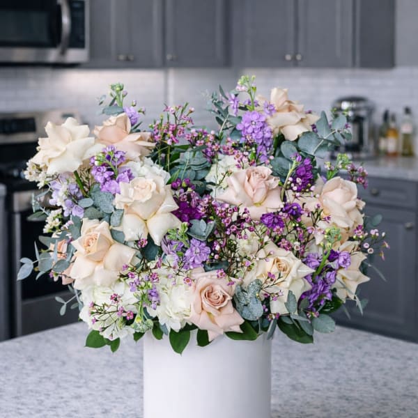 Cream and purple rose arrangement in a white cylindrical vase