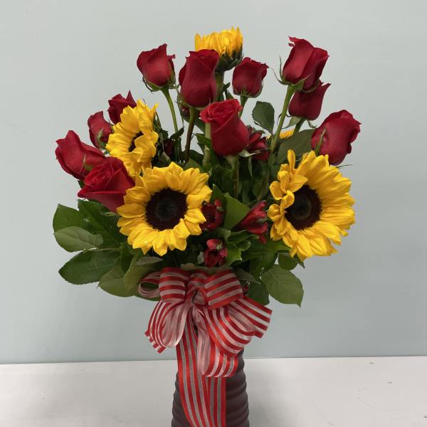 Red roses and sunflowers arranged in a dark vase with a striped ribbon