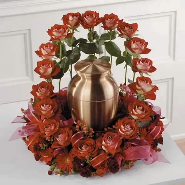 Red roses arranged around a gold urn with pink ribbon accents