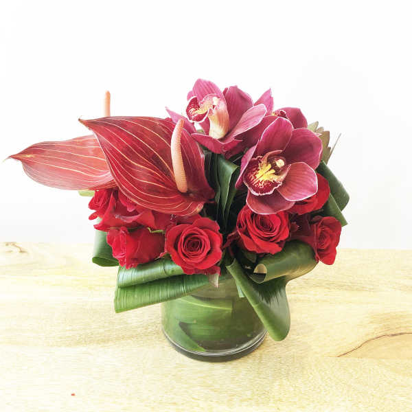 Red roses and pink orchids arranged in a glass vase