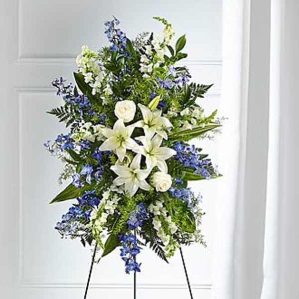 Tall standing spray of white lilies and blue flowers arranged on a metal easel