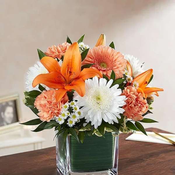 Orange lilies and white daisies in a square glass vase