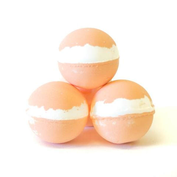 Three peach bath bombs with white bands stacked in a pyramid