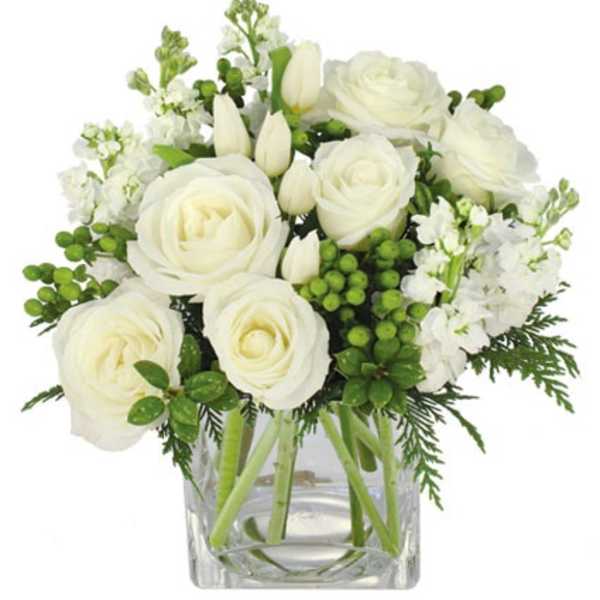 White roses and tulips with green berries arranged in a clear glass cube vase.