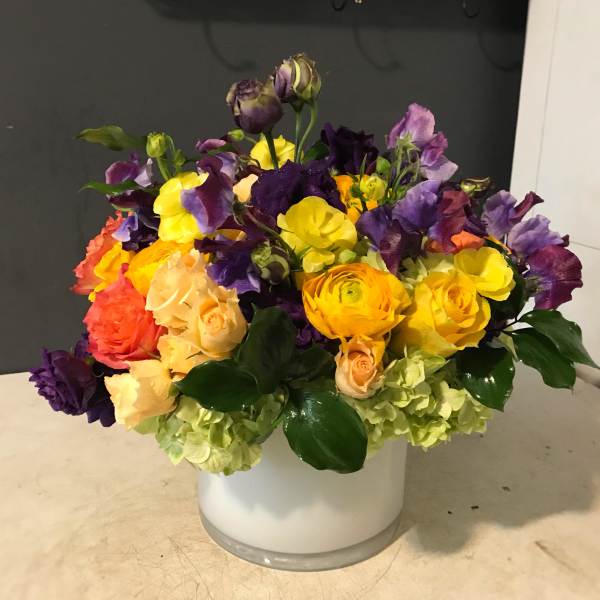 Colorful bouquet of roses and purple blooms in a white vase