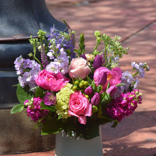 Colorful pink and purple flower arrangement in a white ceramic vase outdoors