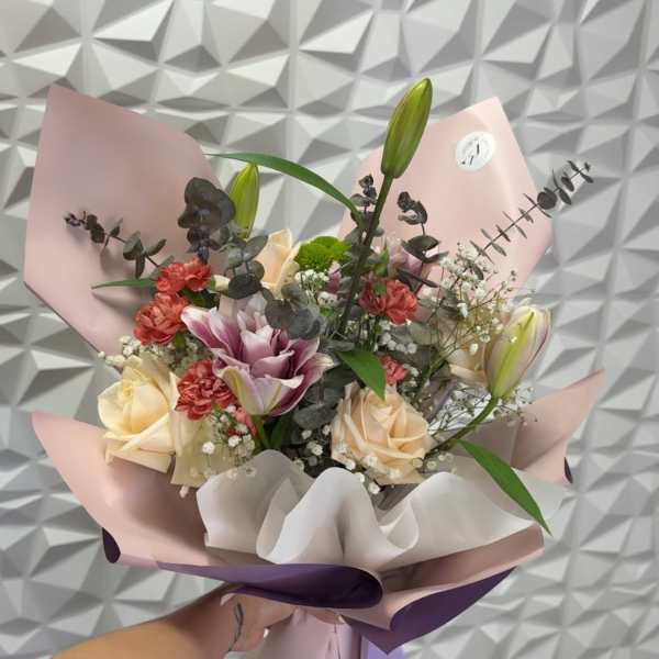 Handheld bouquet of roses, lilies, and carnations wrapped in pink and purple paper