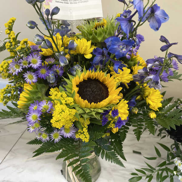 Bouquet with a sunflower center, purple and yellow flowers in a glass vase