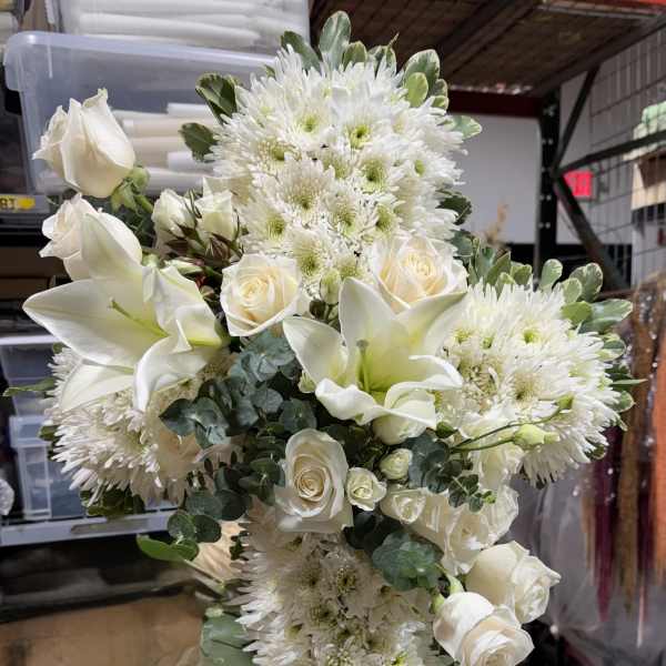 White roses, lilies, and chrysanthemums arranged in a tall spray with a white ribbon.
