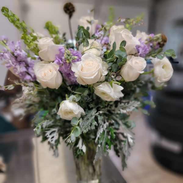 White roses and purple flowers arranged in a glass vase