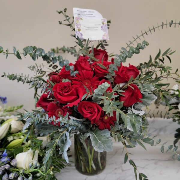 Red roses and gerbera daisies in a glass vase with airy eucalyptus