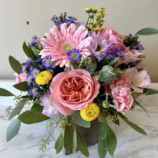 Mixed pink and purple flower arrangement in a square vase