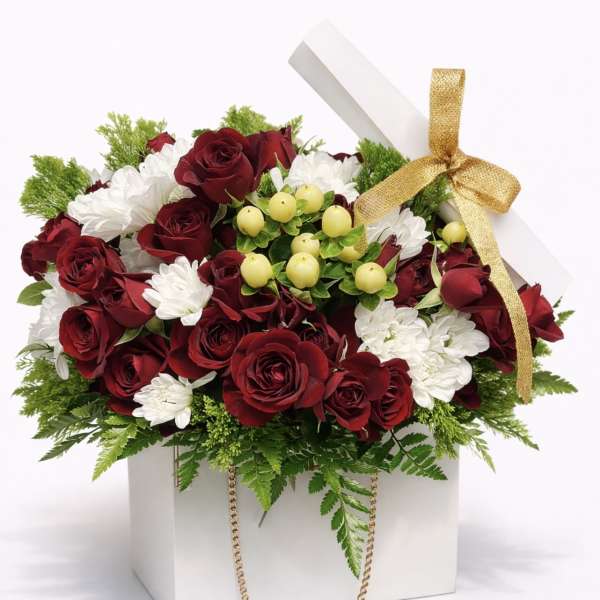 Red roses and white daisies in a white gift box with a gold ribbon