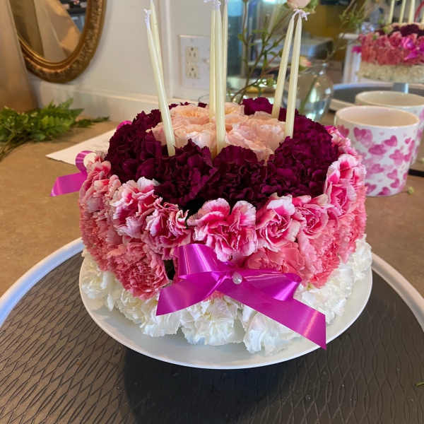 Round floral cake with pink and white carnations and tall candles