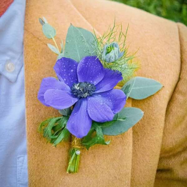 Purple flower boutonniere with eucalyptus on a tan jacket lapel