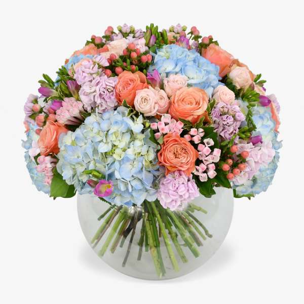 Pastel bouquet of roses, hydrangeas, and small pink flowers in a round glass vase