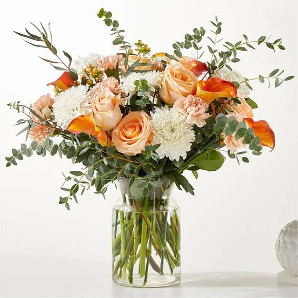 Peach roses and white mums in a clear glass vase with eucalyptus