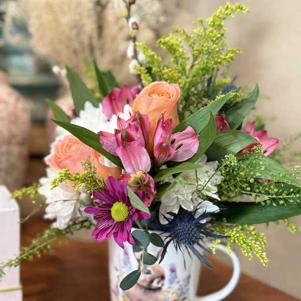 Mixed bouquet in a printed mug vase with pink, peach, and white flowers