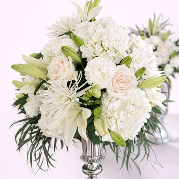 White floral arrangement in a silver vase with lilies and roses