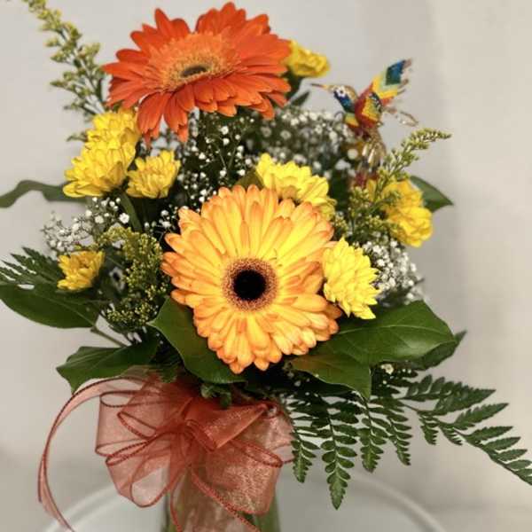 Orange and yellow gerbera daisies in a glass vase with a ribbon