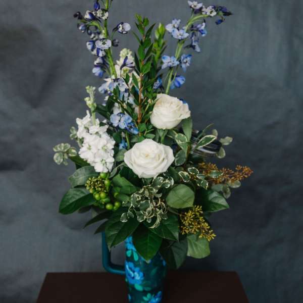 White roses and blue flowers arranged in a tall blue vase