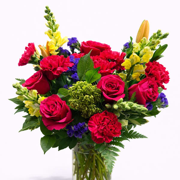 Mixed bouquet of red roses, carnations, and yellow snapdragons in a glass vase