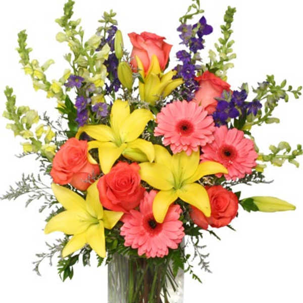 Mixed bouquet of yellow lilies, pink gerbera daisies, and roses in a clear glass vase