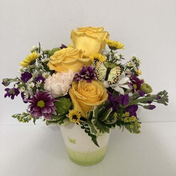 Yellow roses and purple daisies in a white vase with a butterfly accent