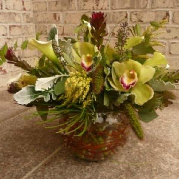 Low arrangement of green cymbidium orchids and pale calla lilies in a clear glass bowl vase