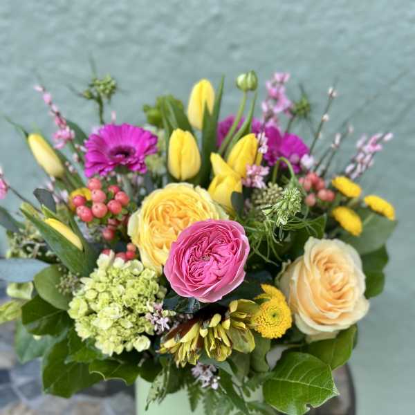 Mixed bouquet of yellow tulips, pink gerberas, roses, and hydrangea in a light green vase