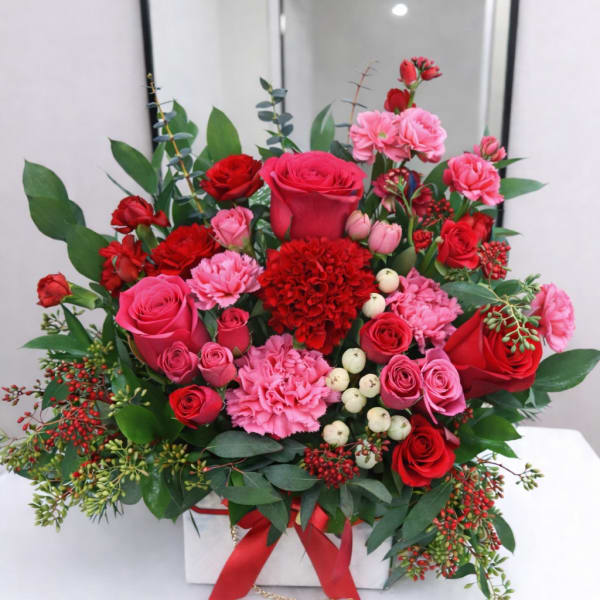 Red and pink roses arranged in a white box with greenery.