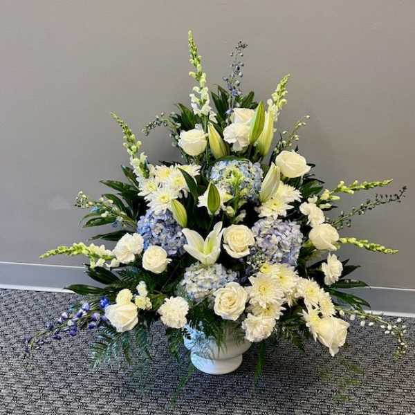 White and pale blue floral arrangement in a white urn vase