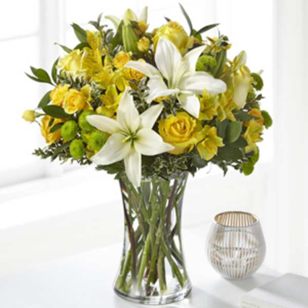 Yellow and white bouquet with lilies and roses arranged in a clear glass vase