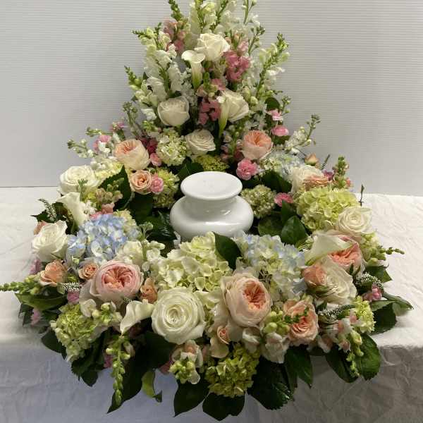 Large white and pastel floral funeral arrangement around a white urn