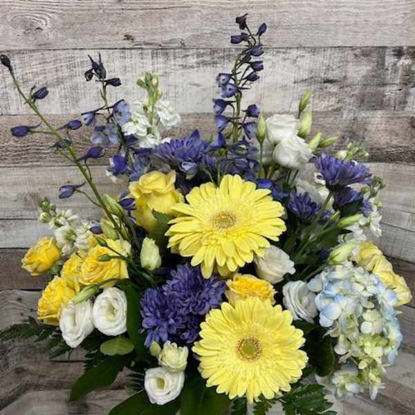 Bouquet of yellow gerbera daisies, blue flowers, and white blooms in a glass vase
