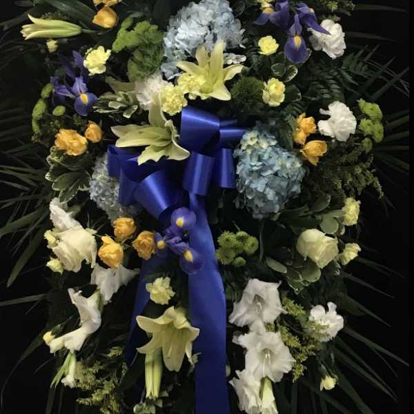 Standing floral wreath with lilies, roses, hydrangeas, and a blue ribbon