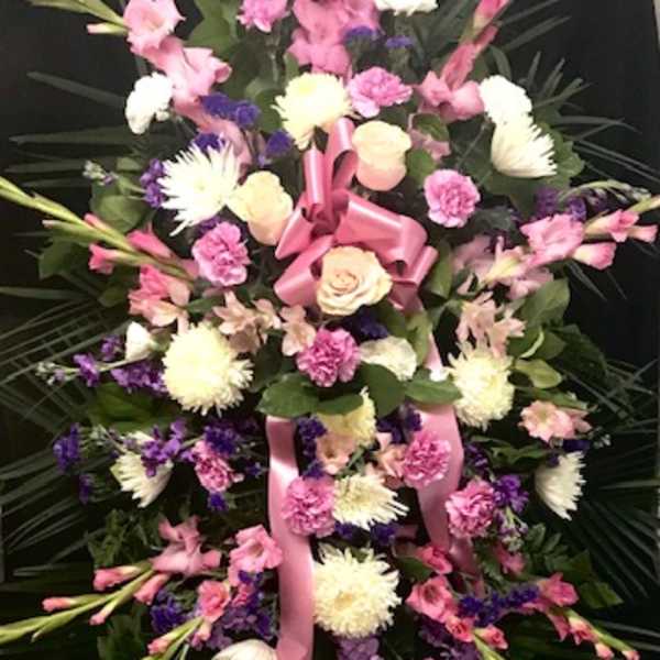 Large pink and white floral standing spray with ribbon on a dark backdrop