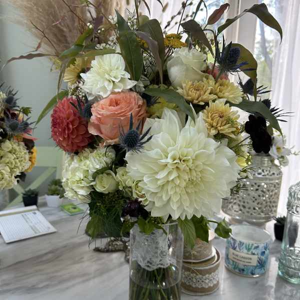 Mixed bouquet with white dahlias, peach roses, and yellow mums in a glass vase