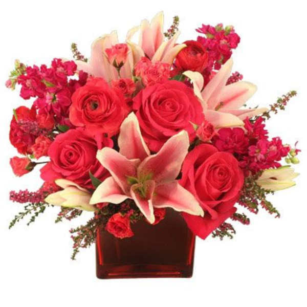 Red roses and pink lilies arranged in a red glass vase