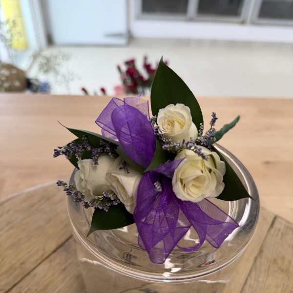 Small bouquet of white roses with purple ribbon in a clear container