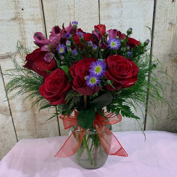 Bouquet of red roses and purple flowers in a glass vase with a red ribbon