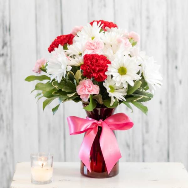 Bouquet of white daisies and red carnations in a red vase with a pink ribbon