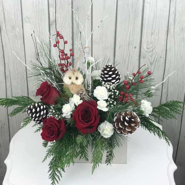 Holiday arrangement with red roses, pinecones, and berries in a white container