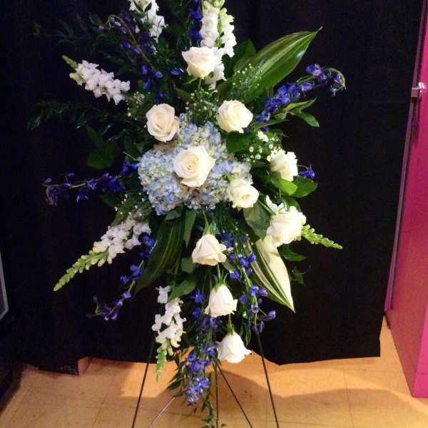 Tall standing floral spray with white roses and blue flowers on a black backdrop
