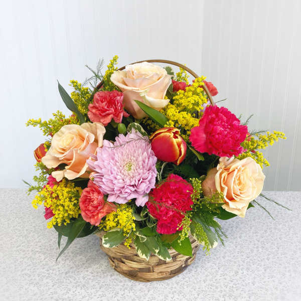 Basket arrangement of peach roses, pink carnations, and a lavender chrysanthemum