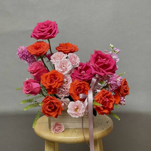 Bright pink and orange rose bouquet with a pink ribbon in a wooden box
