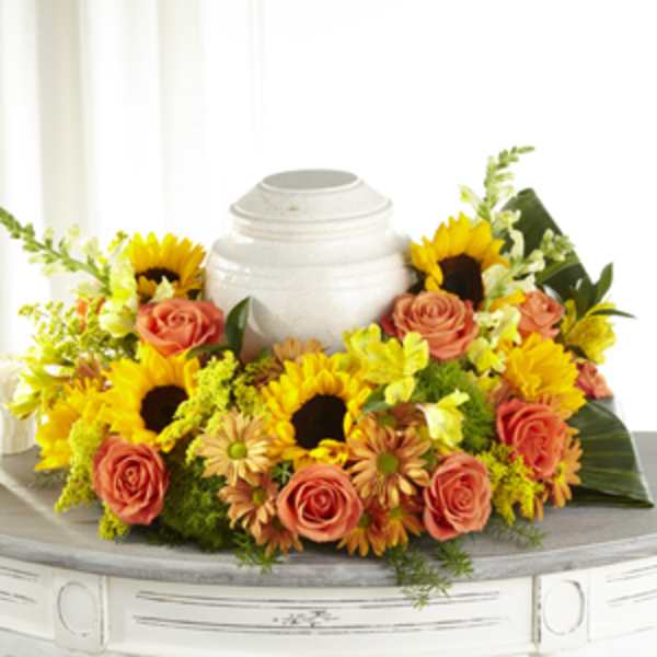 Sunflower and coral rose arrangement around a white urn