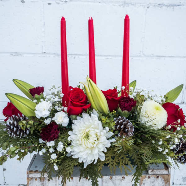 Holiday centerpiece with red candles, roses, white blooms, and pinecones