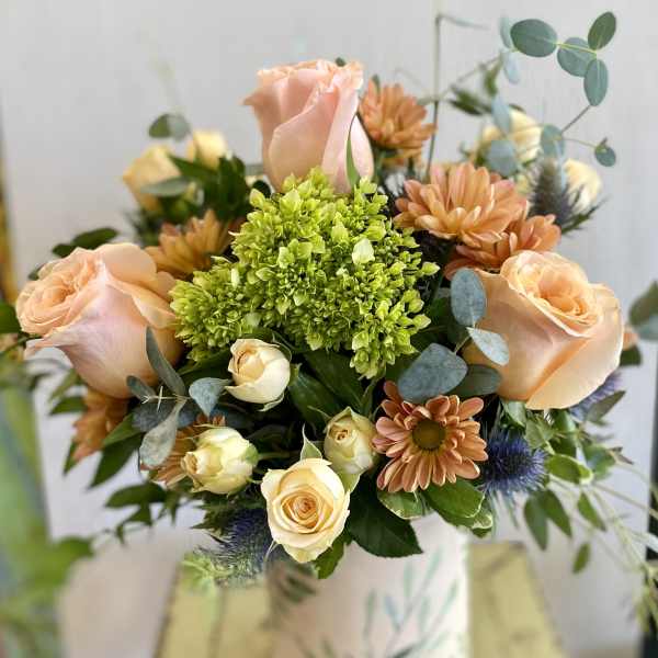 Peach roses and orange daisies in a patterned vase
