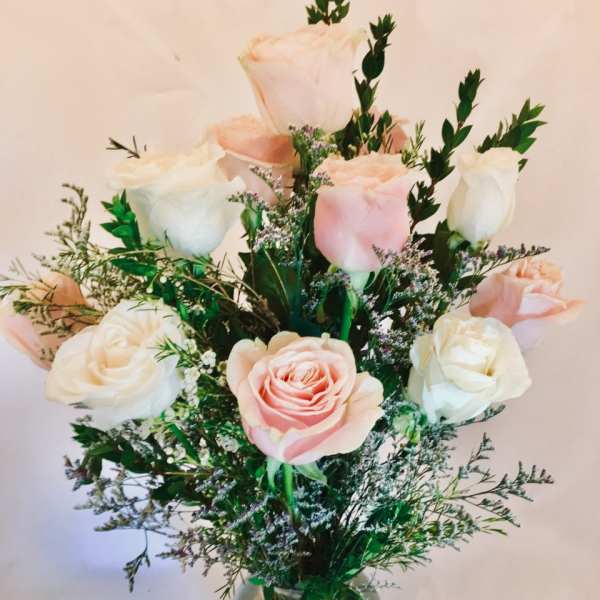 Arrangement of pink and white roses with filler flowers in a clear glass vase tied with a ribbon